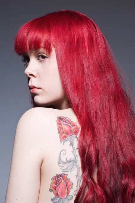 Young woman with long red hair and tattoo, studio shot