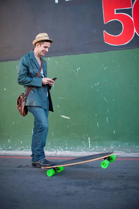 Mid adult male skateboarder reading text message on smartphone