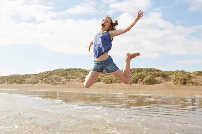 Girl jumping mid air on beach, Camber Sands, Kent, UK