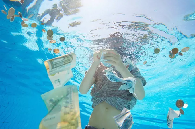 Underwater view of boy in swimming pool grabbing euro currency