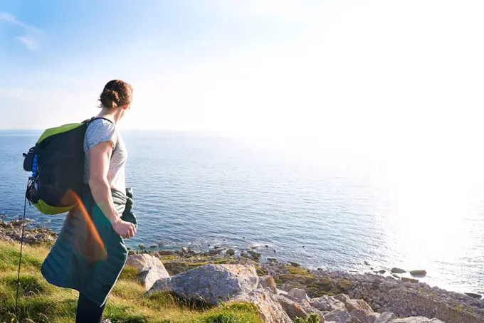 Hiker with backpack on cliff looking at view of ocean, Portland, UK