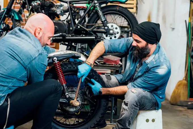 Two mature men, working on motorcycle in garage