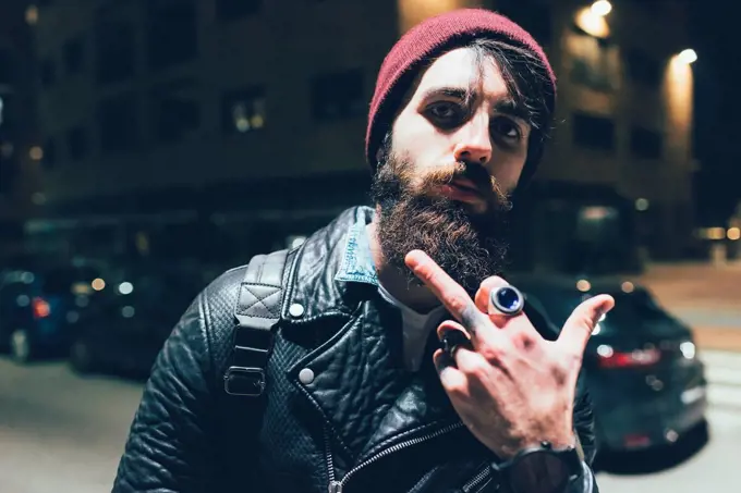 Portrait of young male hipster on city street at night giving obscene finger gesture