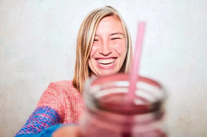 Portrait of woman holding drink towards camera, laughing