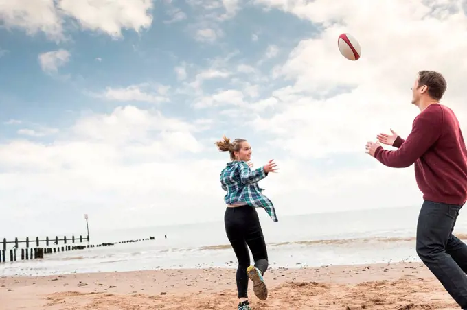 Father and daughter playing rugby on beach