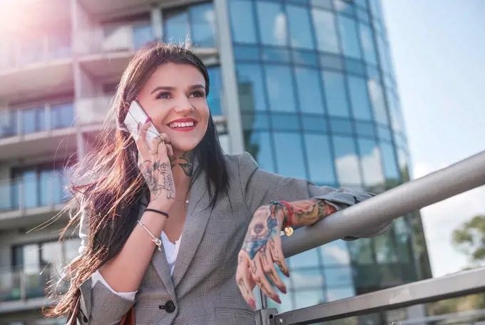 Businesswoman outdoors, using smartphone, smiling, tattoos on hands