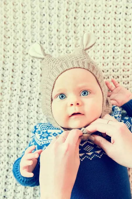 Mother's hands fastening baby sons knitted hat with ears
