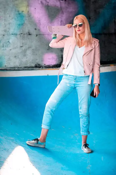 Portrait of young blond female skateboarder wearing sunglasses on skateboard ramp