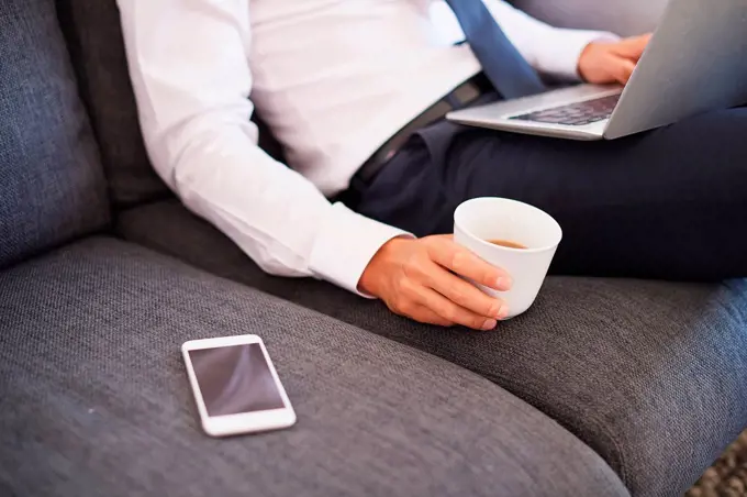 Mid section of businessman sitting on sofa using laptop