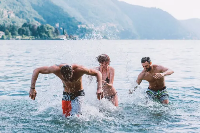 Three young adult friends play fighting in lake Como, Como, Lombardy, Italy