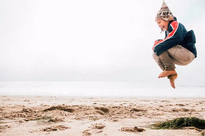 Young boy on beach,jumping, mid air