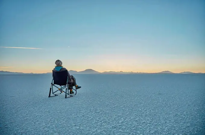 Woman sitting in camping chair, on salt flats, looking at view, Salar de Uyuni, Uyuni, Oruro, Bolivia, South America