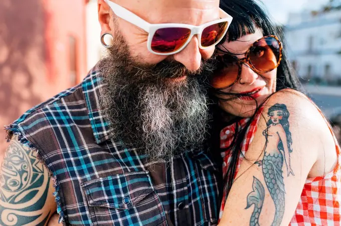 Mature tattooed hipster couple embracing on sidewalk, close up