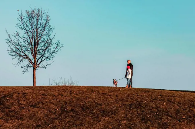 Father and daughter walking dog on hillside