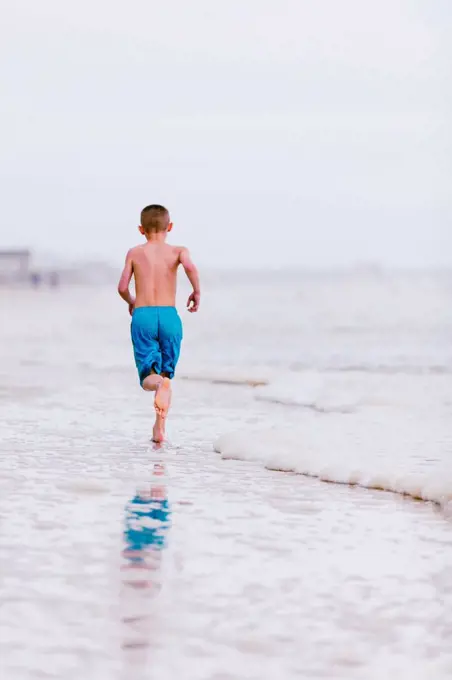 Boy running along water's edge at beach, rear view, Dauphin Island, Alabama, USA