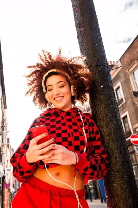 Portrait of young woman outdoors, wearing headphones, holding smartphone