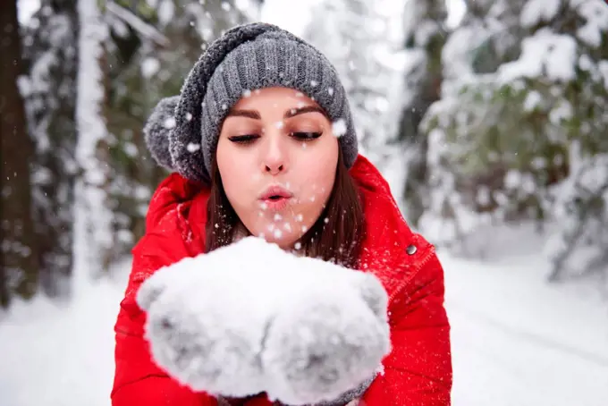 Young woman blowing snowflakes off hands