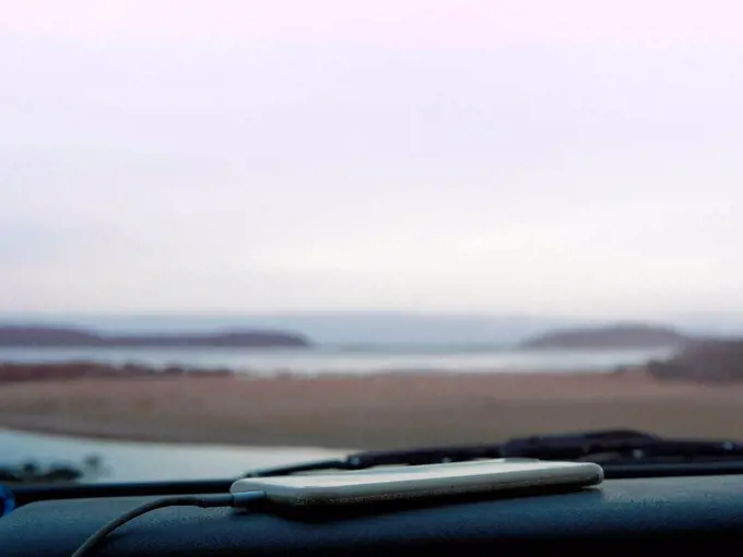 Smartphone on car dashboard, coastal view seen through car windscreen, Broulee, New South Wales, Australia