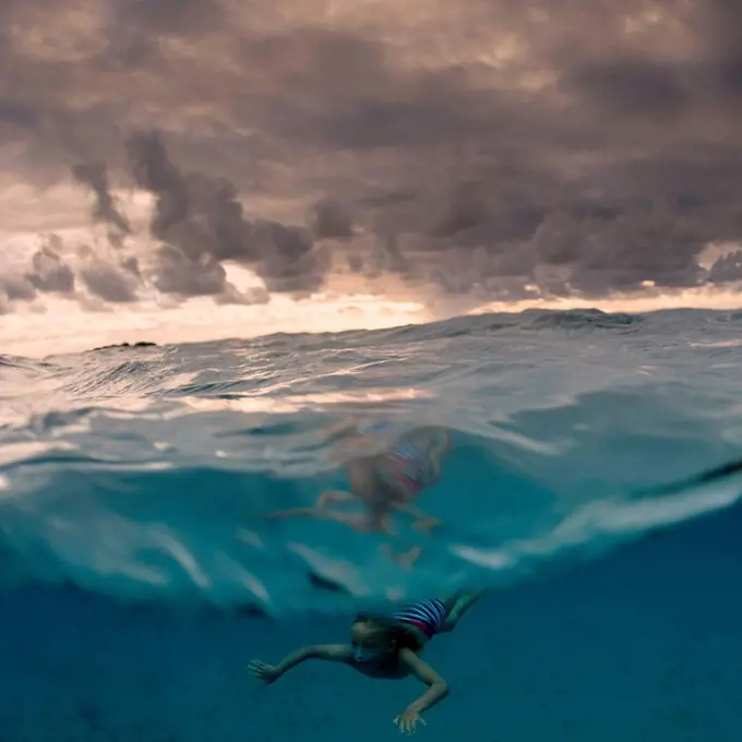 Young boy swimming underwater, split view, Tonga