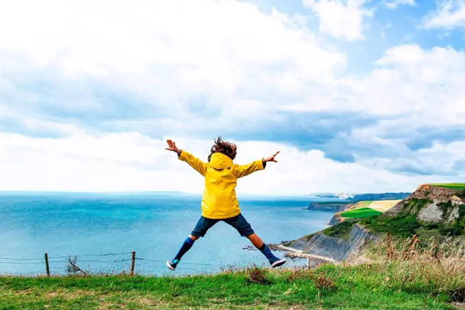 Boy jumping on clifftop by sea, Bournemouth, UK
