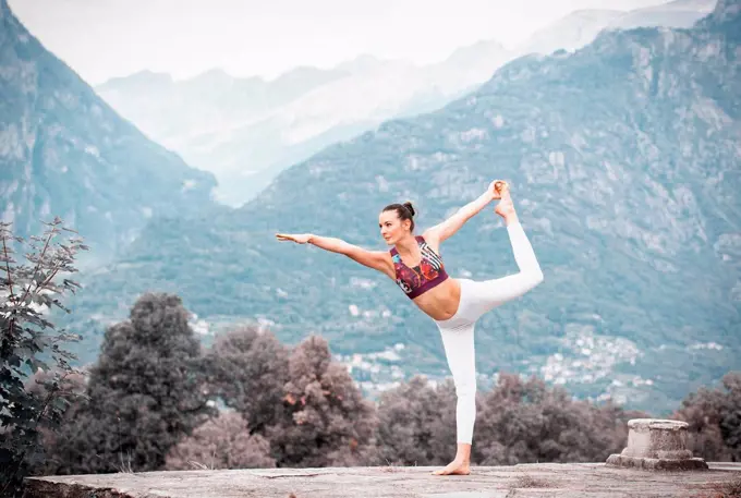 Woman practicing yoga, balancing on one leg in mountain landscape, Domodossola, Piemonte, Italy