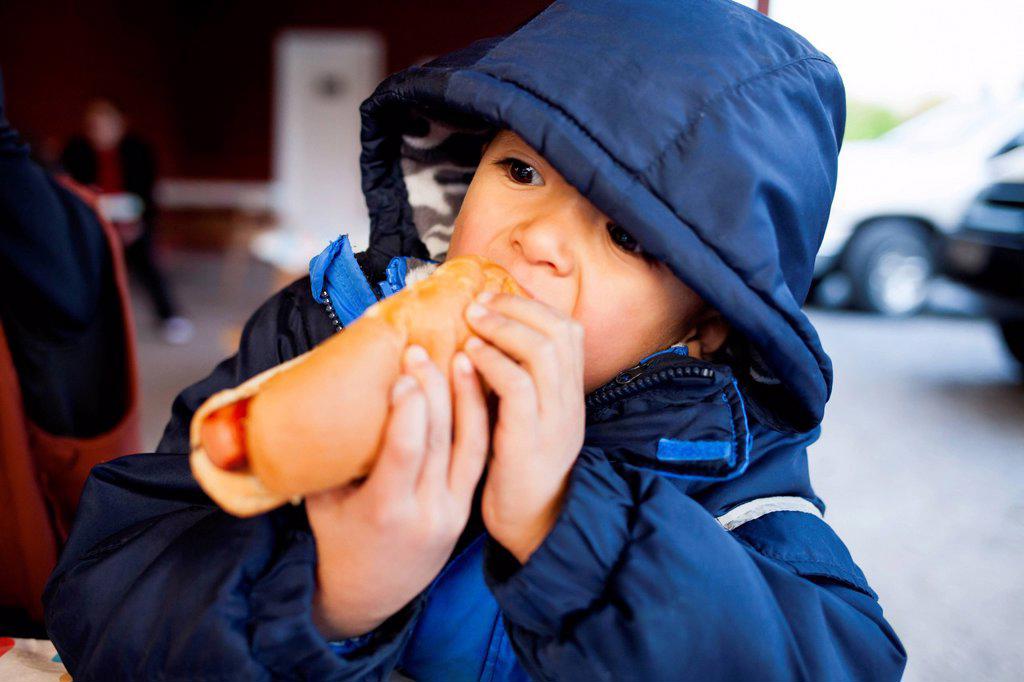 A 4 year old Japanese American boy eats a hot dog.