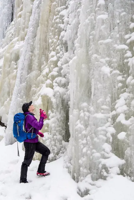 A woman hiker looking up at a tall wall of ice and snow.
