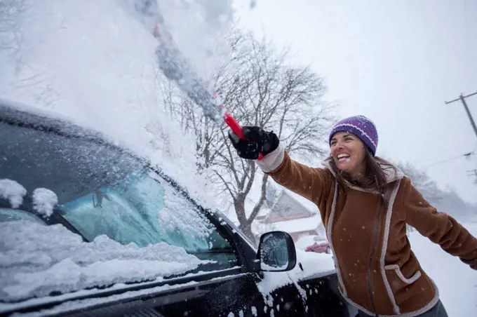 An Adult Woman Having Fun Clearing Off Her Vehicle After A Fresh Blanket Of Snowfall