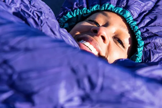 Portrait of young woman lying in purple sleeping bag and smiling at camera, Newburyport, Massachusetts, USA