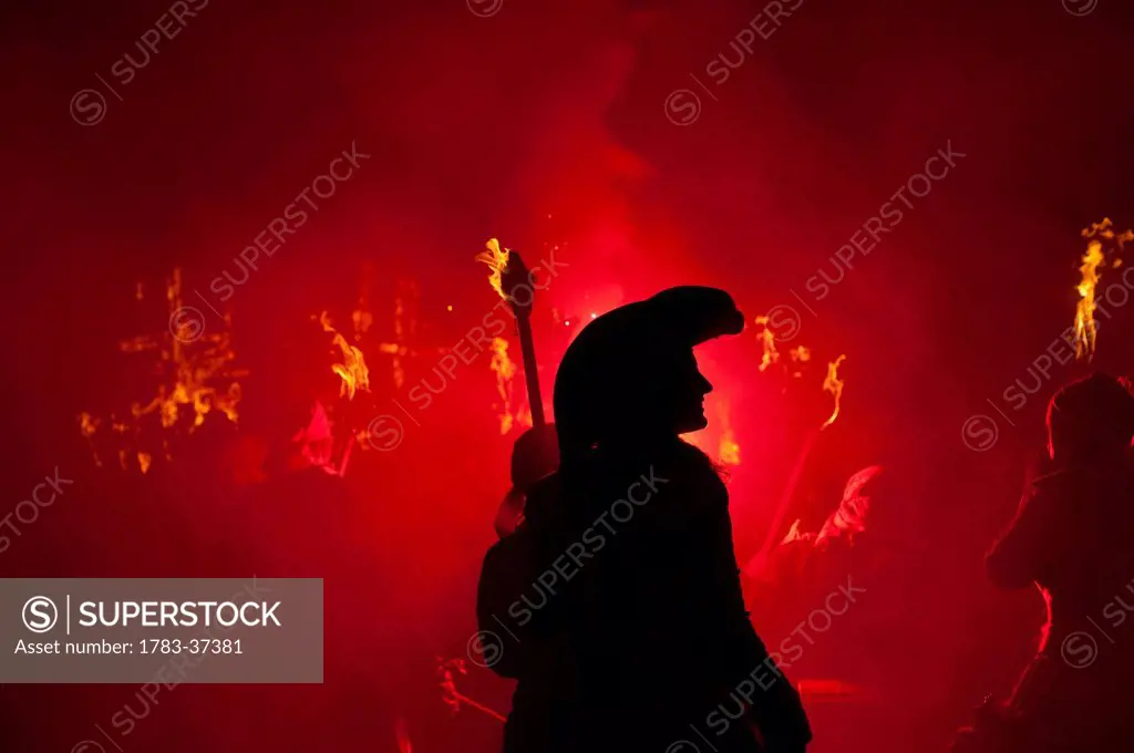 Silhouette of pirate with burning torch from Southover Bonfire Society lit by red flares on United Grand Procession down High Street, Bonfire Night; L...