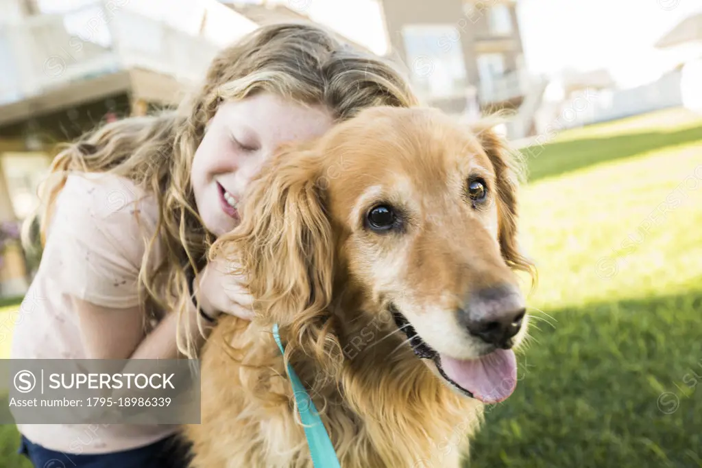 Girl (10-11) hugging Golden Retriever outdoors