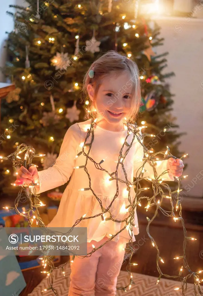 Little girl (4-5) wrapped with christmas lights in living room