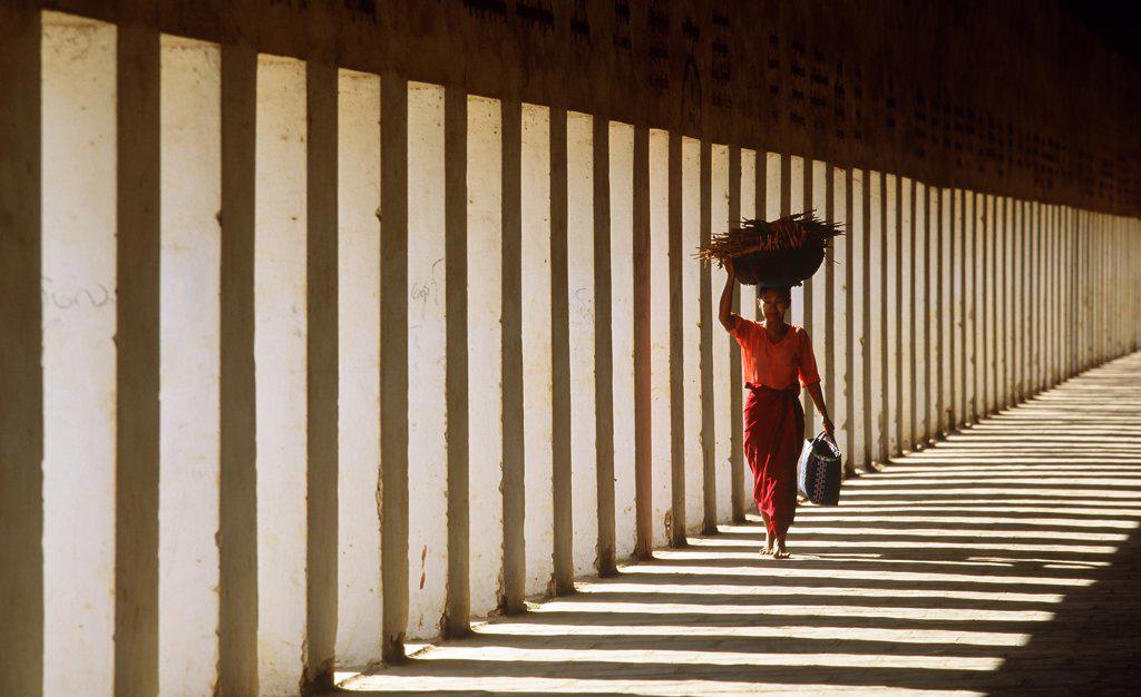 Myanmar, Bagan, Mandalay Division, Woman walking in portico of Schwezigon Pagoda carrying wood on her head