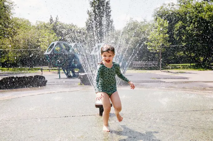 USA, New York, New York City, Girl playing next to water sprinkler on playground