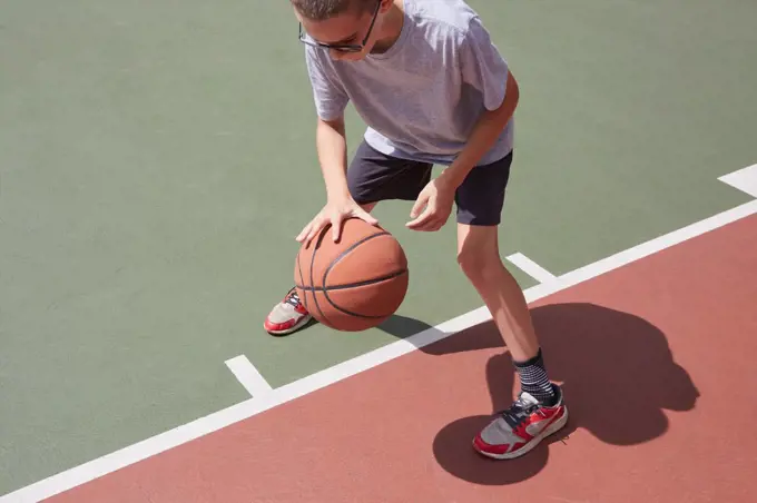 Boy (8-9) dribbling basketball in park