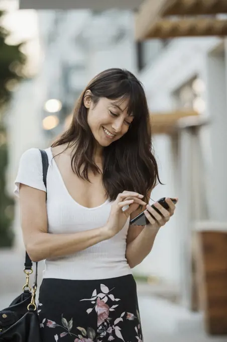 Smiling woman looking at smart phone in city