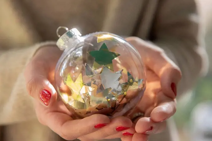 Hands of woman holding Christmas bauble with star shape confetti