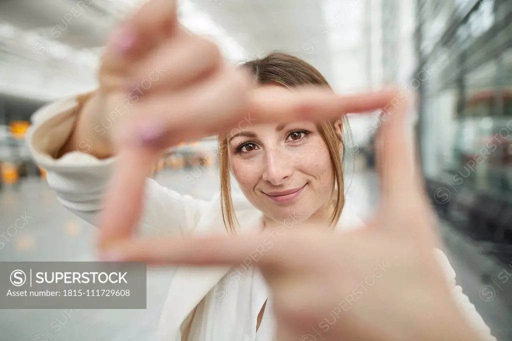 Portrait of smiling young businesswoman doing finger frame at the airport