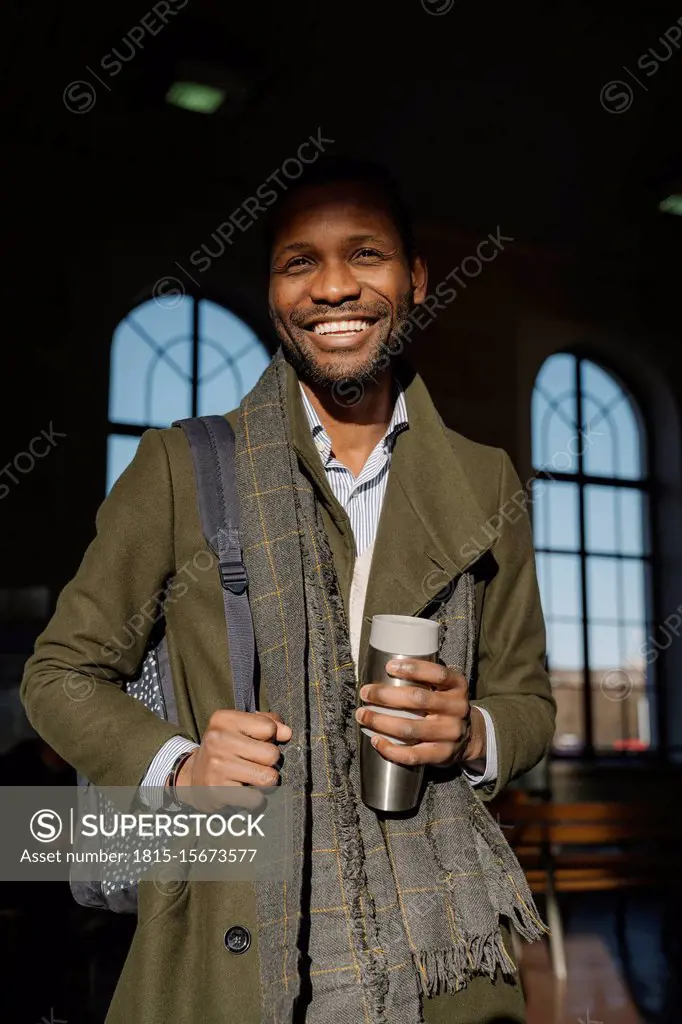 Portrait of happy stylish man with reusable cup in the train station
