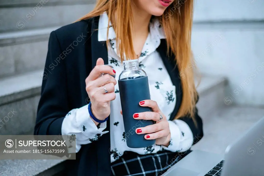 Close-up of businesswoman sitting on stairs with laptop and reusable bottle