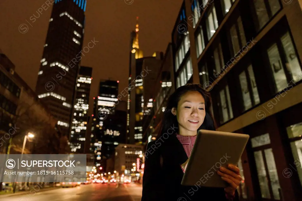 Young woman using tablet in the city at night, Frankfurt, Germany
