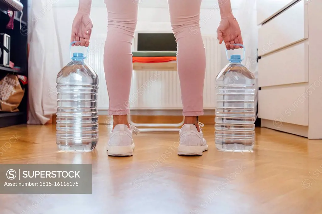 Low section of woman practicing weightlifting with water bottles at home