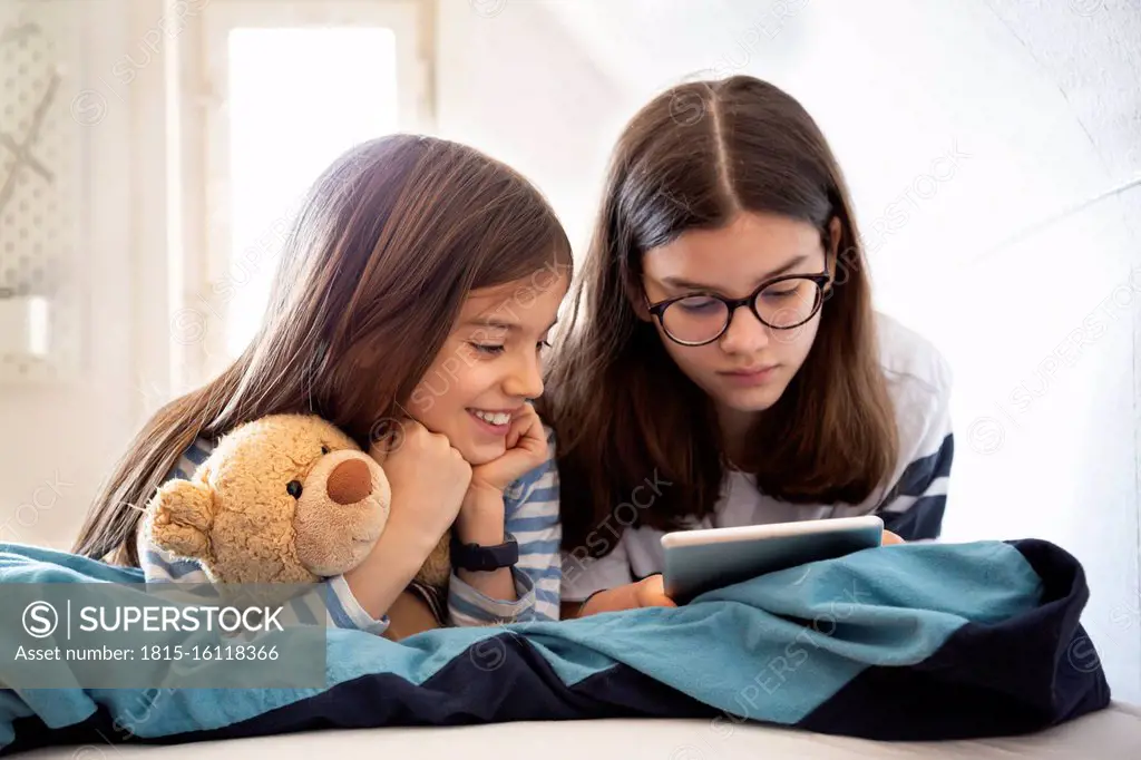 Sisters using tablet lying on bed