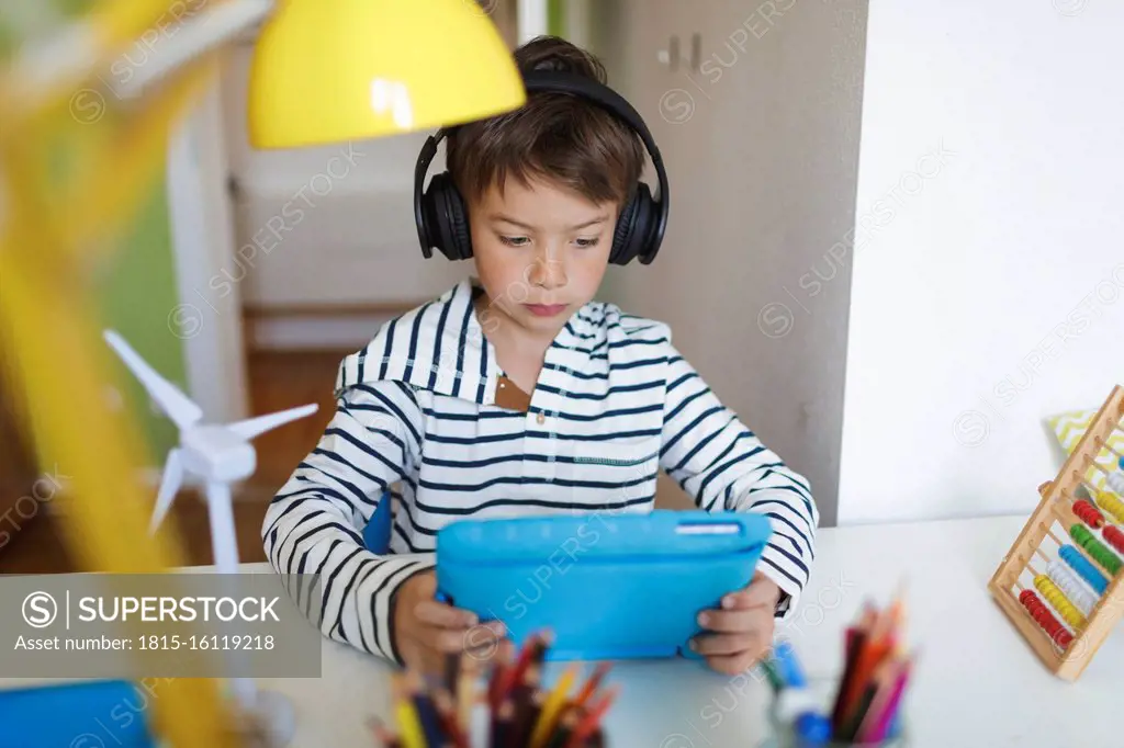 Boy doing homeschooling and using tablet and headphones at home