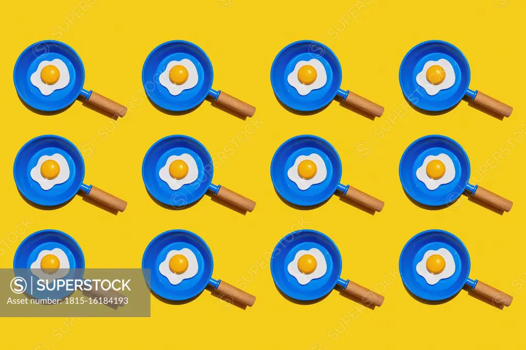 Pattern of rows of fried eggs on blue pans against yellow background