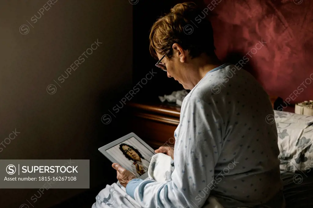 Senior woman in bedroom discussing over video call with doctor at home