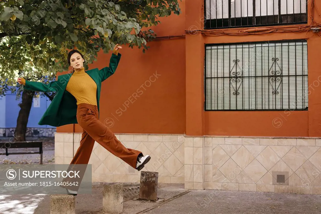 Beautiful woman wearing green jacket climbing on bollard in city