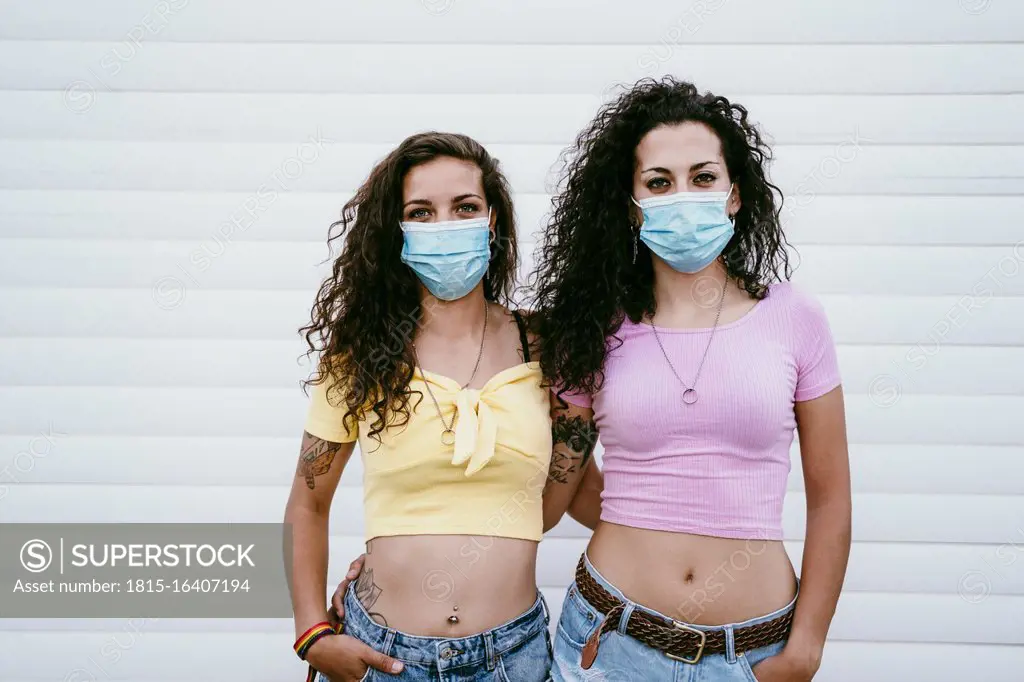 Lesbian couple wearing masks standing against wall in city
