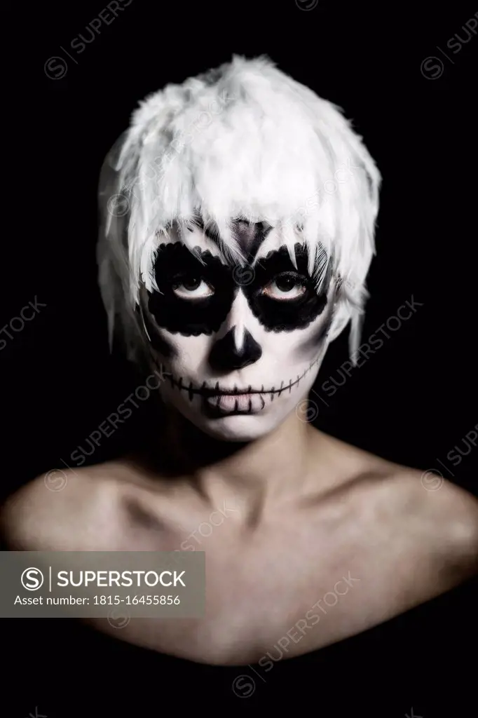 Portrait of woman with skull make-up wearing headgear of white feathers, studio-shot