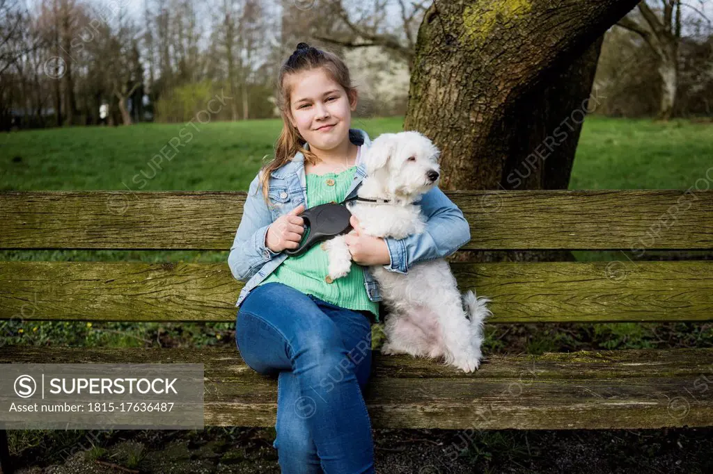 Smiling girl with dog sitting on bench in park